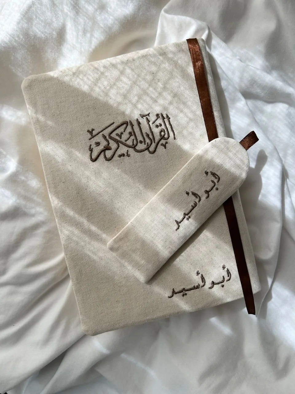 Off-white cotton book cover, Al-Quran Al-Karim calligraphy and Arabic name embroidered in chocolate brown, brown ribbon and matching fabric bookmark