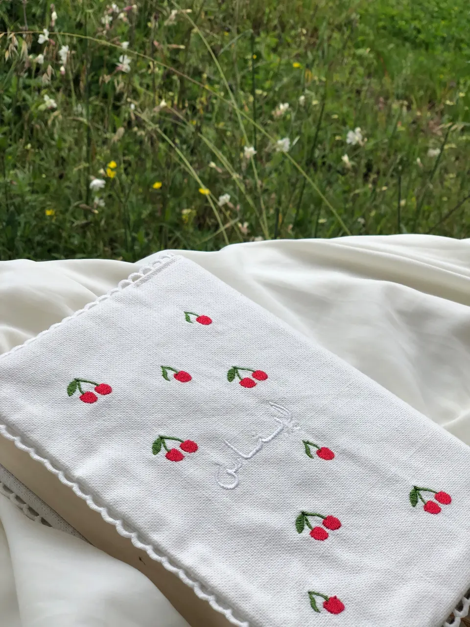White cotton book cover scattered with red embroidered cherries, Arabic name embroidered white on white, white crown lace